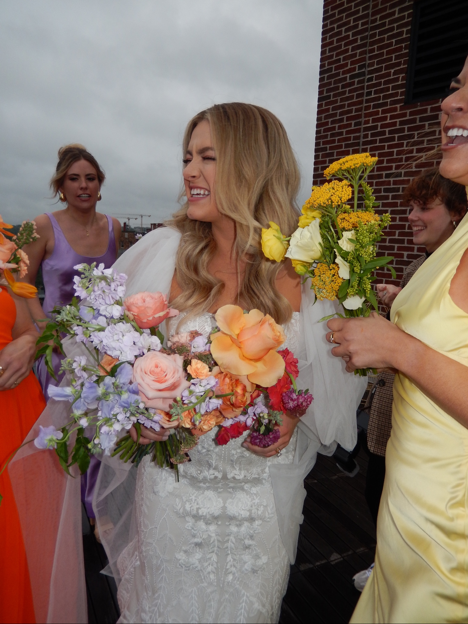 Bride laughing with bridesmaids wearing colorful dresses and carrying florals during wedding content creation
