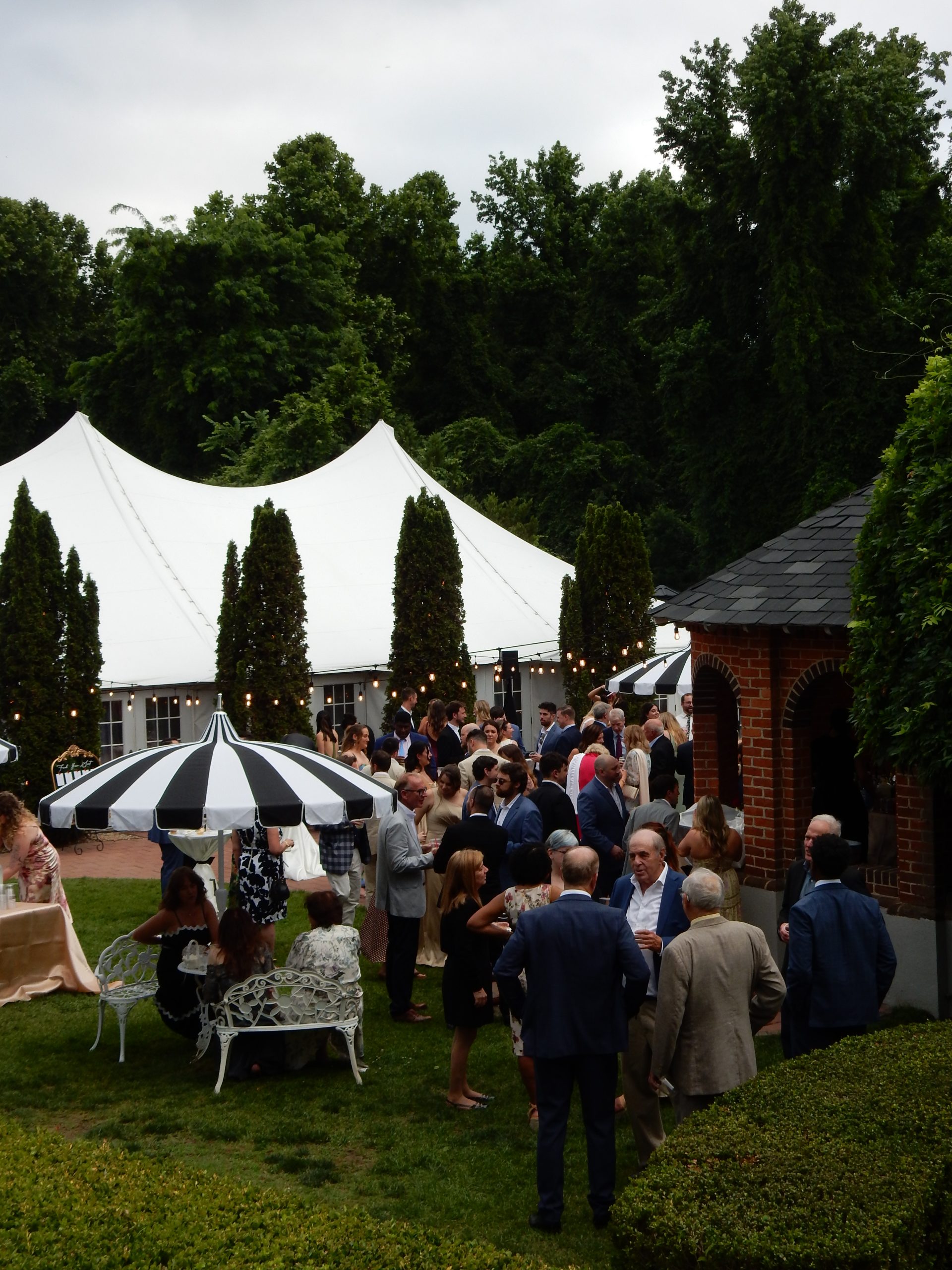 wedding cocktail hour in the garden at mankin mansion with a white tent in the background and a striped umbrella in the foreground