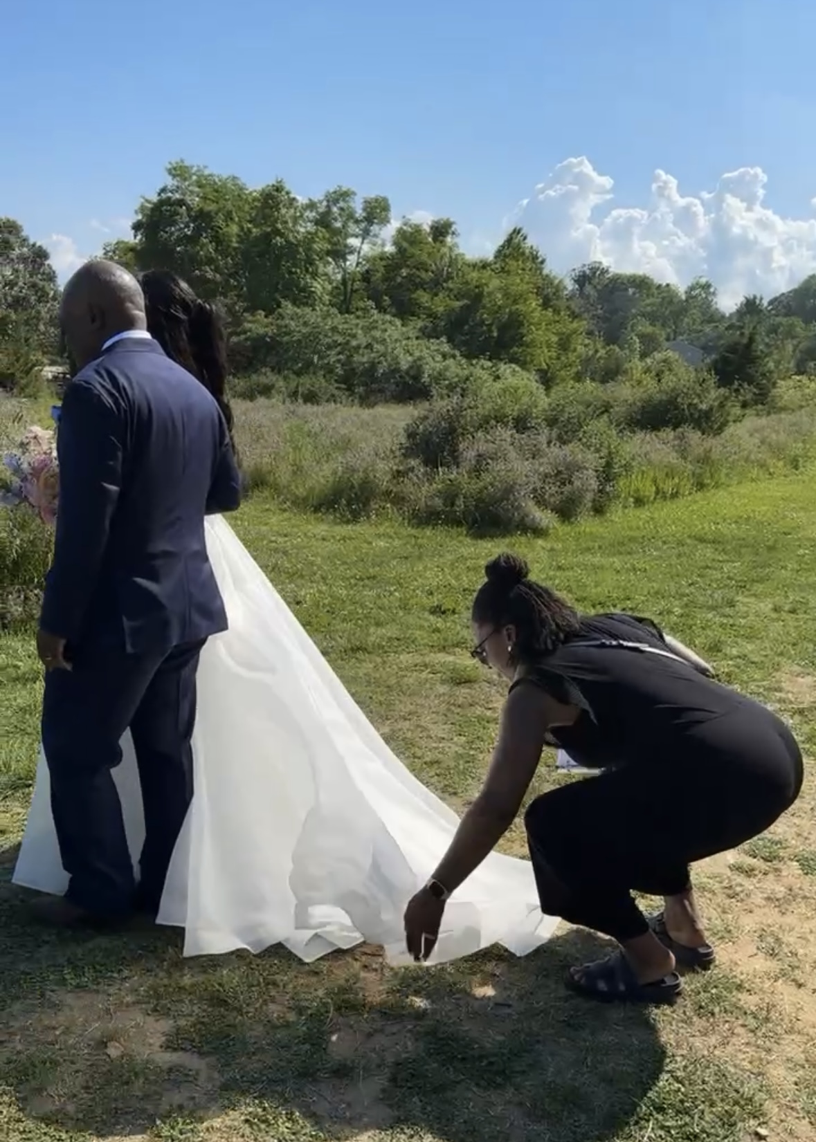 wedding planner fixing bride's dress train before she walks down the aisle